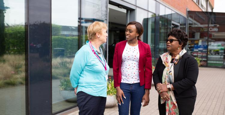 Three women standing outside a hospital talking Three women standing outside a hospital talking