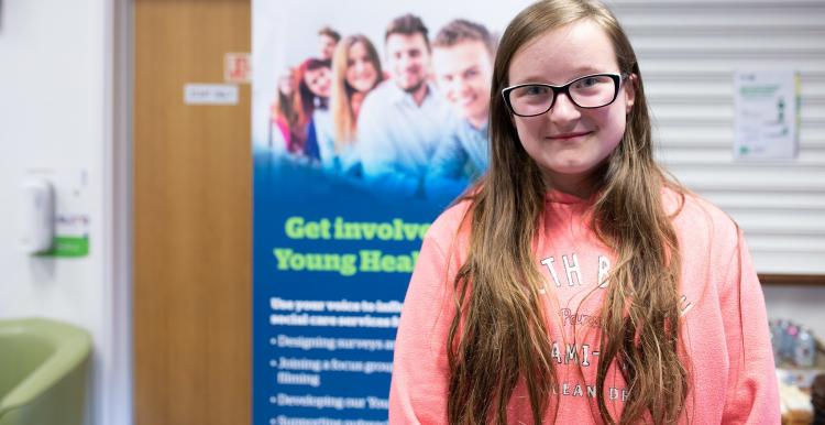 Teenage girl wearing glasses in front of a Healthwatch banner