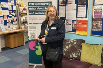 Healthwatch Rochdale Community Project Worker standing in front of a Healthwatch banner in The Lighthouse Project