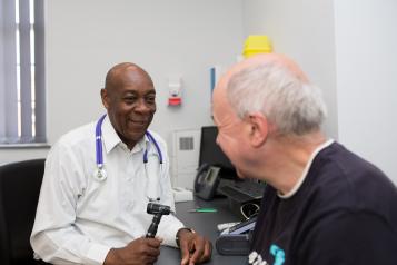 GP speaking to a patient, about to use a thermometer