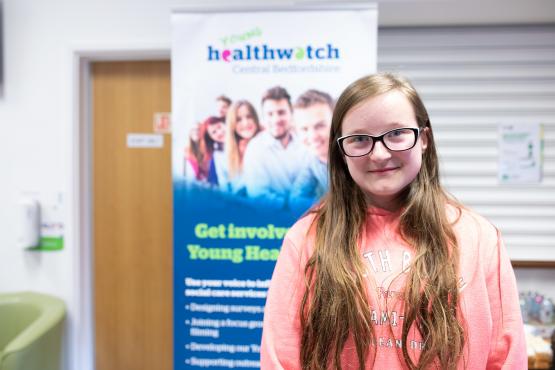 Young girl standing in front of a Healthwatch sign Young girl standing in front of a Healthwatch sign